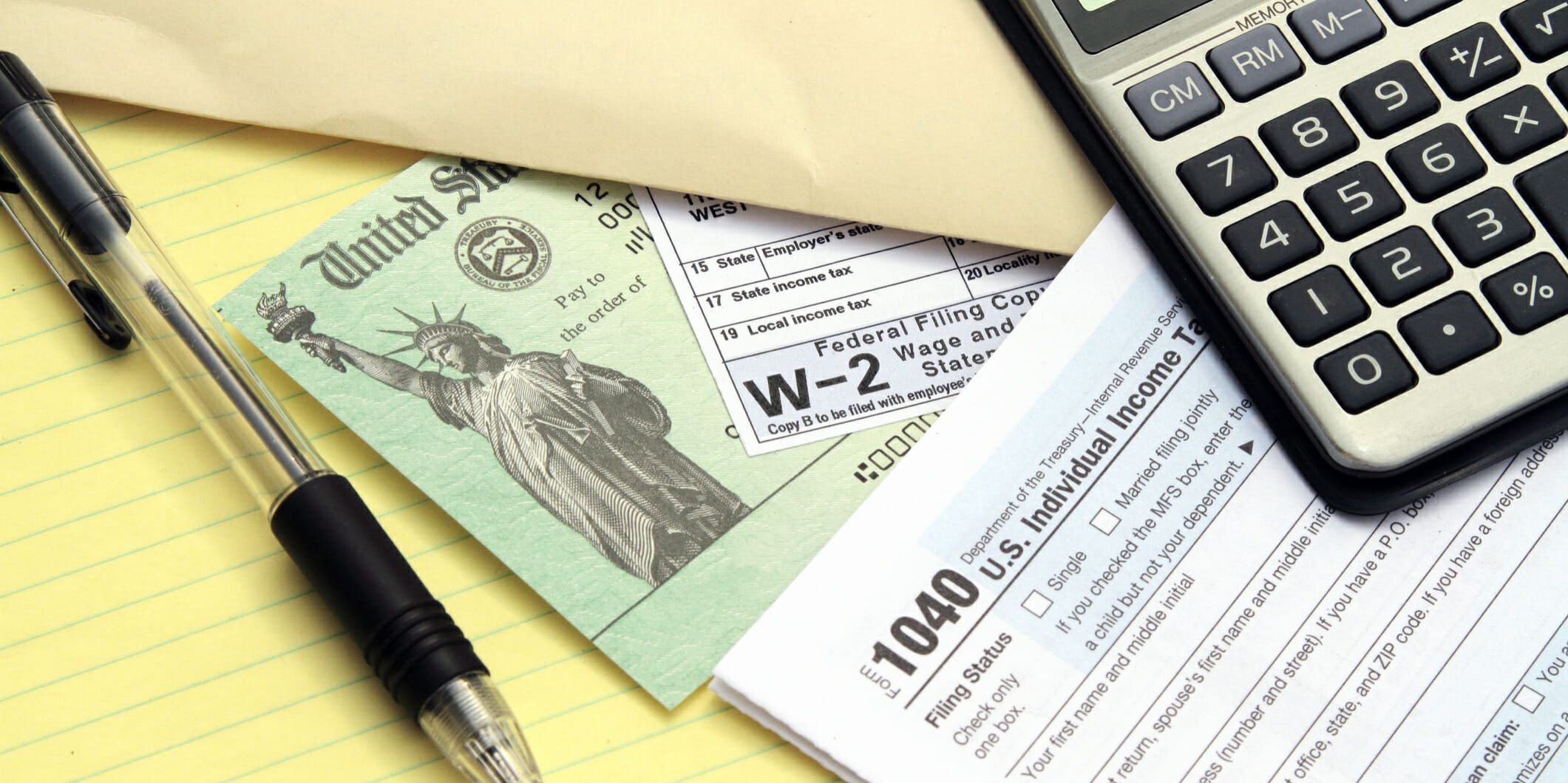 Tax forms with Treasury check. IRS tax forms 1040 and W-2. Tax preparation concept. Treasury check represents a tax refund. Calculator, pen and papers yellow note pad also visible.